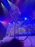 A circus performer navigates a spinning metal apparatus under colorful stage lights with a snowy village backdrop.