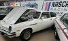 A classic white car with its hood open is displayed in a showroom alongside other vintage vehicles.