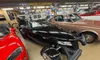 A collection of classic and vintage cars is displayed in a showroom with automotive memorabilia and decorations on the walls.