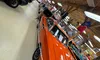 A collection of vintage cars is displayed in a wooden-ceilinged showroom, featuring a prominent orange car in the foreground.