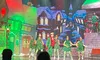 A festive holiday performance features dancers in Christmas-themed costumes on stage with a backdrop of a snowy village.