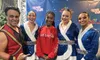 A group of five people, including a man in a red costume and three women in blue sequined outfits, pose with a girl in a red sweatshirt in a festive setting.