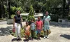 A group of four happy children with an adult posing for a photo on a sunny day at a location that seems to be a park or a zoo, with lush green trees and Spanish moss in the background.