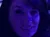 A group of people are seated in a theater, illuminated by purple lighting, with a woman taking a selfie in the foreground.