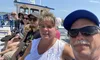 A group of people are smiling for a selfie on a bright sunny day aboard a boat with a clear blue sky in the background.