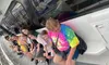 A group of people, including someone in a colorful tie-dye shirt, are lined up and leaning against the wall of a boat.