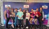 A group of performers in colorful costumes poses with three people in front of a 
