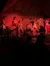 A group of performers is engaged in a traditional dance or cultural performance on a stage with red lighting, in front of an audience who are sitting at tables.