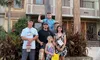 A group of six people is posing for a photo in front of a building with a sign that reads
