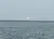 A large pinkish sun hangs low over the horizon above a rippled body of water with a hint of land in the distance.