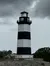 A monochrome-striped lighthouse stands under a cloudy sky, imparting a serene and somewhat solemn atmosphere.