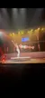 A pair of performers are executing an acrobatic routine on a circular stage under vibrant stage lighting.