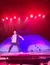 A performer energetically holds a newspaper on a brightly lit stage with red and purple lighting effects.