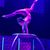 A performer exhibits remarkable flexibility and balance in a contortion act on a circular platform under blue stage lighting.