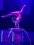A performer exhibits remarkable flexibility and balance in a contortion act on a circular platform under blue stage lighting.
