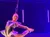 A performer in a futuristic outfit is doing an aerial acrobatics routine against a starry, purple-lit background.