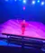 A performer in a red outfit is balancing on a platform under colorful stage lights.