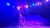 A performer in a vibrant, colorful setting is skillfully handling multiple hula hoops on stage.