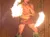 A performer in traditional attire is skillfully spinning fire sticks during a performance, with someone capturing the scene on a smartphone.