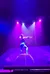A performer in vibrant lighting is balancing on a high circular apparatus while drawing a bow and arrow.