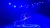 A performer is balancing dynamically inside a large ring on a stage illuminated by blue lighting.