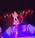 A performer is balancing on a stack of objects on a stage, surrounded by colorful lighting and shadows.