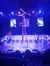 A performer is balancing upside down on a tall stack of chairs on a stage with vivid lighting and two people observing as the audience watches.