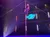 A performer is climbing a tall pole on a stage with colorful lights and starry background.