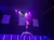 A performer is demonstrating an impressive vertical pole acrobatic skill under vibrant stage lighting.