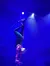 A performer is doing a handstand while holding a bow with her feet, aiming an arrow in a spotlight.