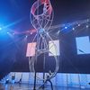 A performer is engaged in a daring acrobatic act inside a giant rotating wheel under blue lighting at a live entertainment event.