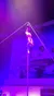 A performer is executing a vertical split high up on a pole under purple stage lighting in front of a backdrop with a snowy village scene.