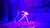 A performer is executing an acrobatic maneuver inside a large hoop on stage with dynamic blue and purple lighting.