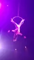 A performer is executing an acrobatic pose suspended from an aerial hoop under vibrant stage lights.