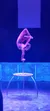 A performer is executing an impressive contortion pose on top of a pole, backlit by a purple stage light.