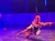 A performer is gracefully suspended in mid-air by a harness, reaching out with one arm on a stage with a starry background.