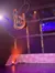 A performer is hanging upside down from a hoop on a brightly lit stage with colorful lighting and a geometric backdrop.