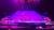 A performer is in a dynamic split pose, skillfully handling multiple hula hoops on a brightly lit stage.