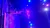 A performer is skillfully balancing and spinning multiple hoops under bright stage lights with a vivid blue and purple ambiance.