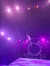 A performer is suspended in the air under vibrant purple stage lights, with a circular frame in the background.