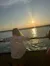 A person gazes out at the water as the sun sets, casting a warm glow and creating reflections on the surface.