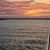 A person is capturing the beautiful sunset over water from the deck of a boat, with colorful clouds scattered across the sky.