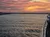 A person is capturing the beautiful sunset over water from the deck of a boat, with colorful clouds scattered across the sky.