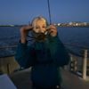 A person is holding a crab in front of their face on a boat at dusk.