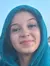 A person is holding a small crab on a shell, smiling at the camera with another individual in the background, and they both appear to be wearing hoodies.