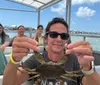 A person wearing sunglasses and a NASA t-shirt is holding up a crab on a boat with several other people seated in the background.