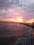 A person with a tattooed arm points towards a vibrant sunset over the ocean.
