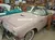 A pink vintage Ford Thunderbird convertible is displayed in a classic car showroom filled with automotive memorabilia.