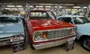 A red vintage Dodge truck is displayed in a car museum with informational signs and other classic cars around it.