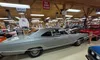 A silver vintage car is displayed in a museum setting, surrounded by various automotive memorabilia and signs.